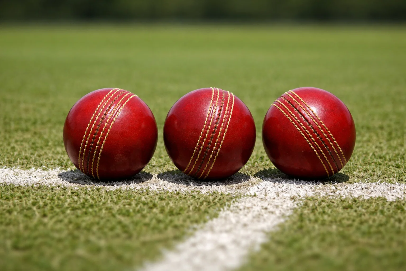 Drie cricketballen naast elkaar op een groene pitch met witte cricketlijnen